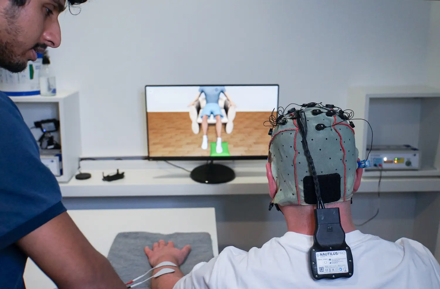 Therapeut begleitet recoveriX-Training mit Bildschirmdarstellung von Gehirnaktivitäten.