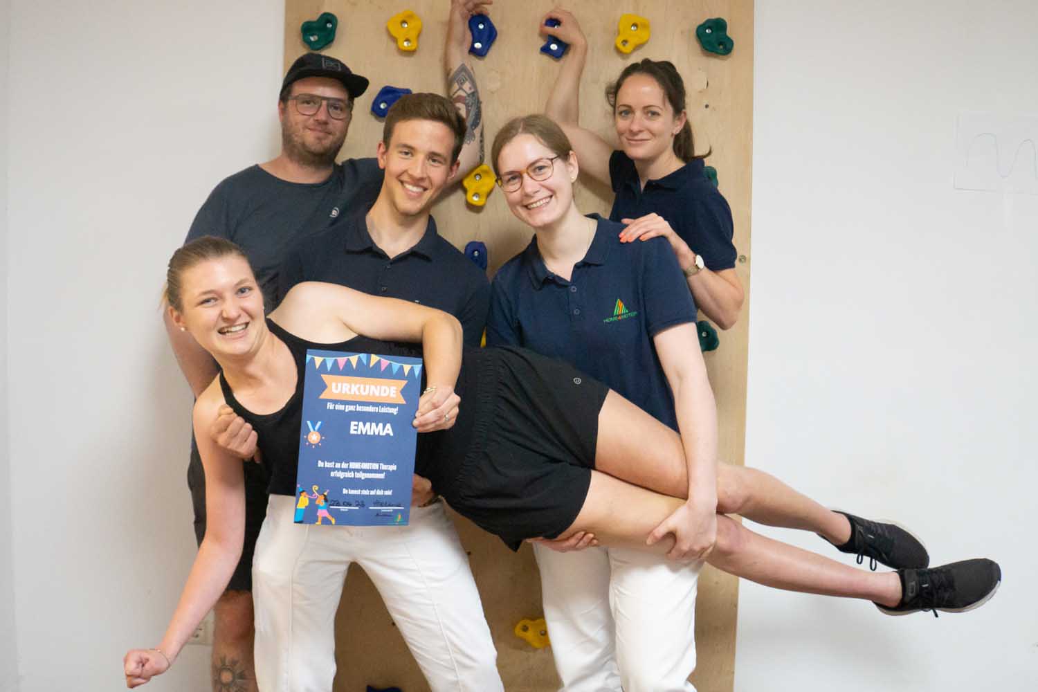 3 Therapeuten, 1 Klient, 2 Therapeuten halten Klientin Emma an Schulter und Beinen